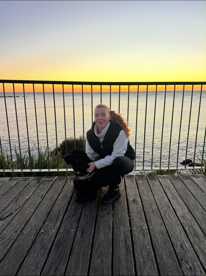 Nicole crouched with a black spaniel at sunrise